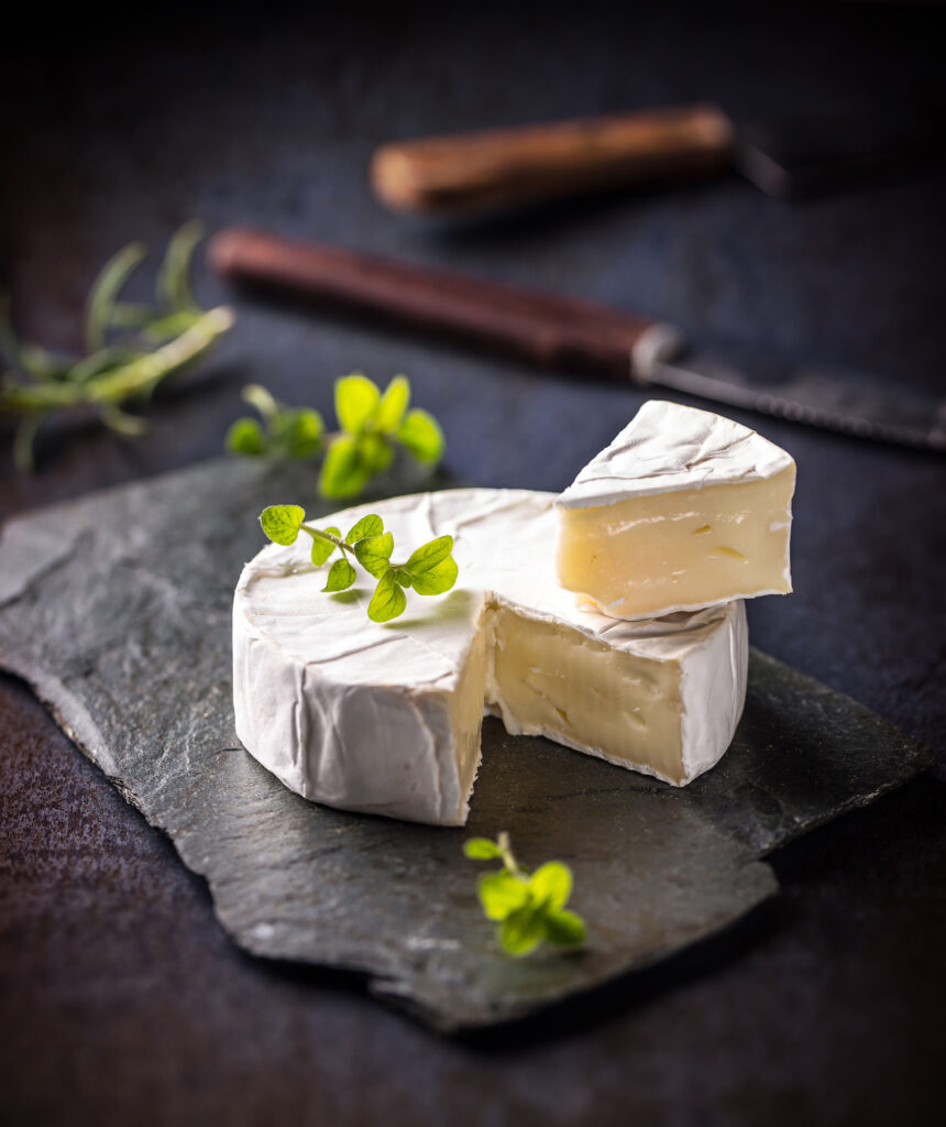 Francuski ser Camembert z Normandii o kremowej konsystencji, podany na kamiennej desce z ziołami.